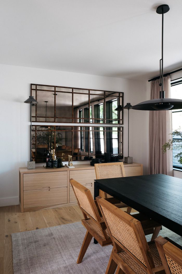 Dining area with a black table and wicker chairs, wooden cabinet, and large antiqued mirror stacked on the wall.