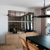 Dining area with a black table and wicker chairs, wooden cabinet, and large antiqued mirror stacked on the wall.