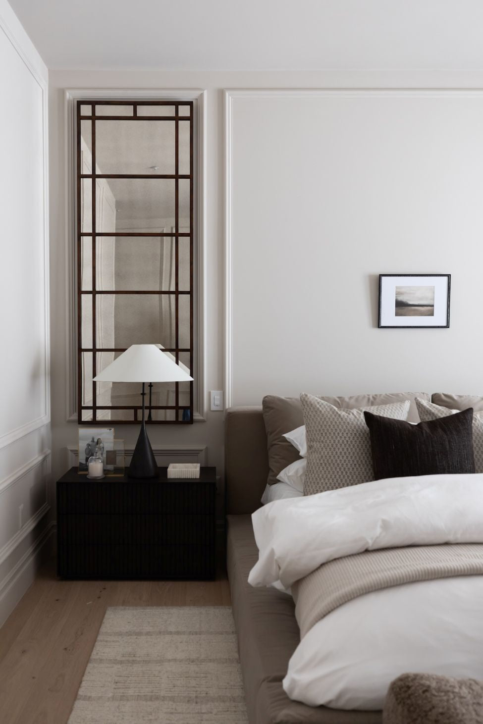 Modern bedroom with an antiqued mirror, bed, nightstand, and lamp.