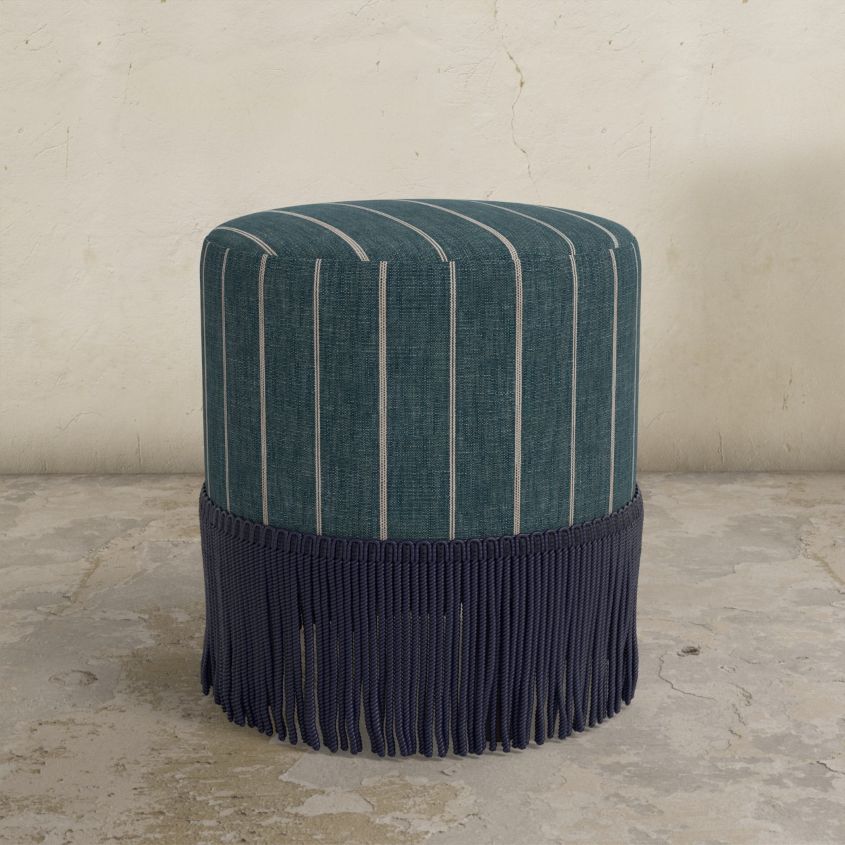 Striped ottoman with fringes on a concrete floor against a beige wall