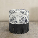 Round ottoman with black and white patterned top and black fringe on a beige background