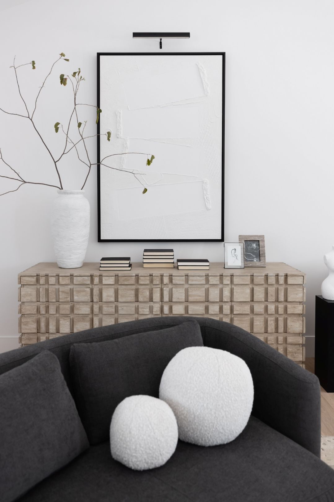 The Oslo dresser with books, photos and a vase and artwork above behind a gray sofa with pillows.