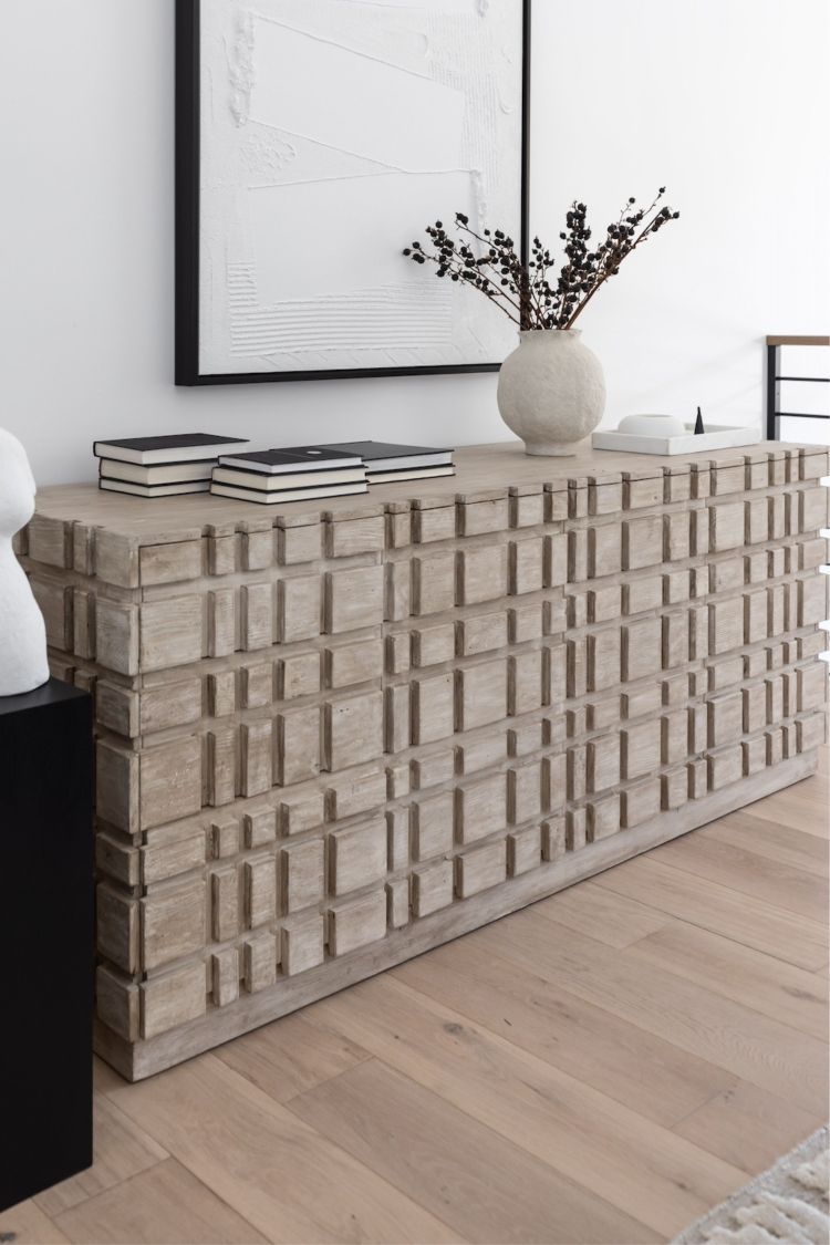 A gray washed Oslo dresser made of reclaimed Douglas Fir wood, featuring a geometric pattern on the front. It is placed in a room with a vase on top and books stacked on the left side.