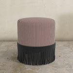 berry red striped upholstered  ottoman with fringe on a concrete floor.