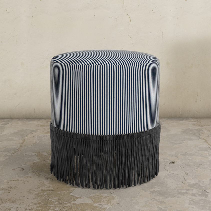 indigo blue striped upholstered ottoman with fringed bottom on a concrete floor