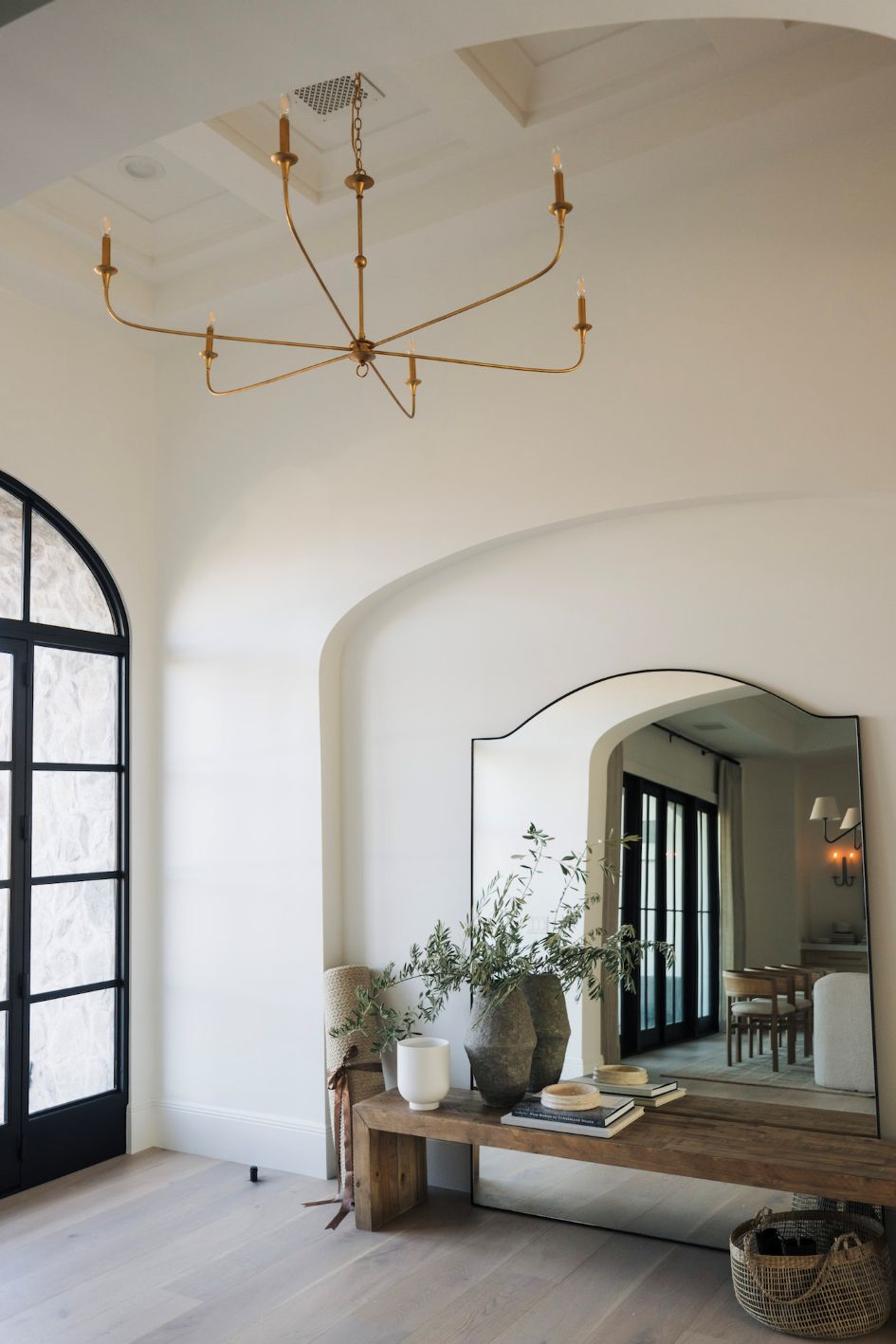 Elegant interior with a gold chandelier, large mirror, and wooden bench.