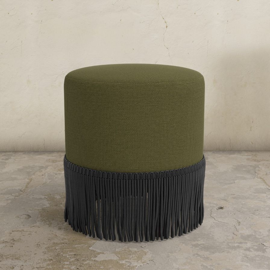 Green upholstered ottoman with black fringe on a stone floor.