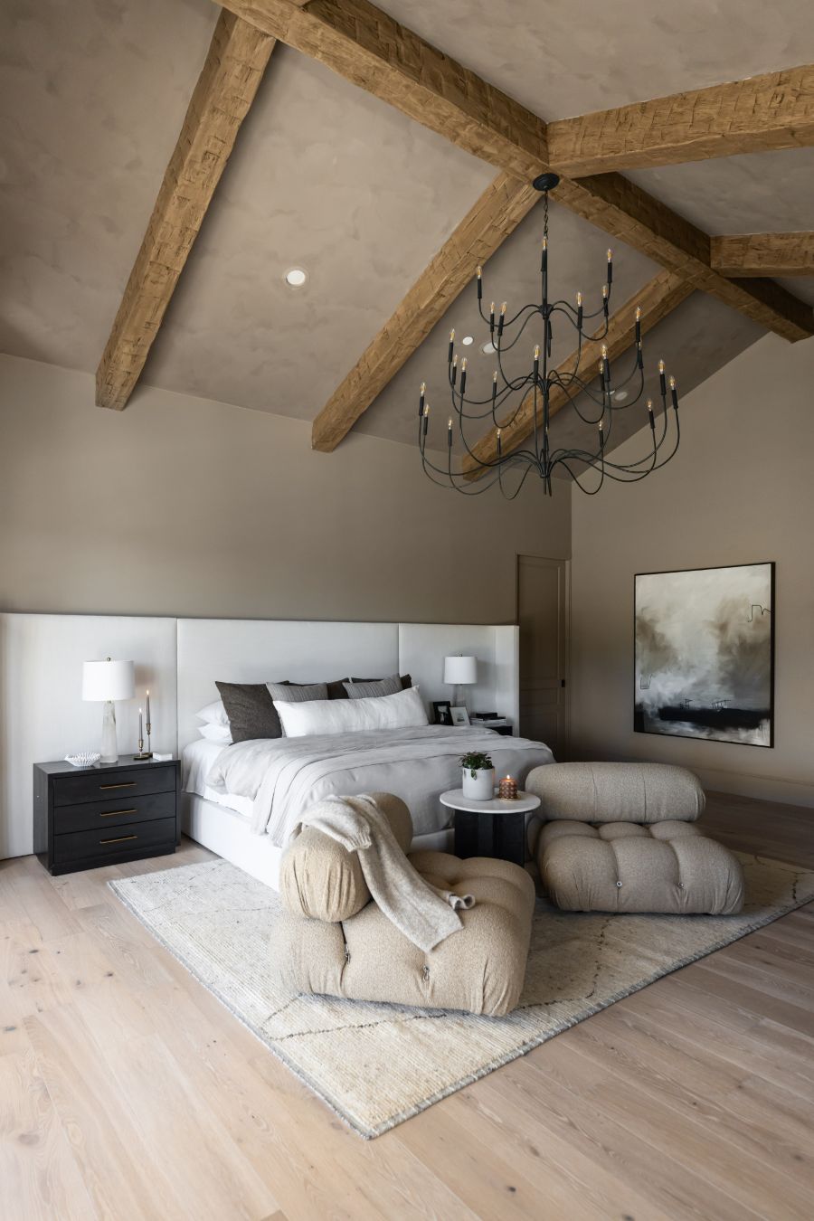 Modern bedroom with wooden beams, a Tirrell Large Black candle style chandelier, and neutral decor.