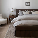 Willa power loomed area rug on the floor with a neatly made bed with decorative pillows in a bedroom setting.