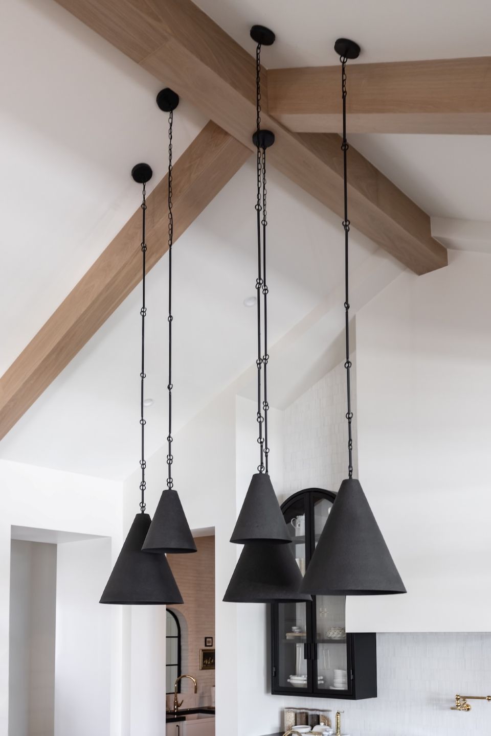 Three black pendant lights in two sizes hanging from the ceiling with wooden beams in the background.