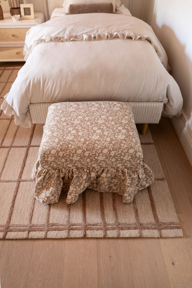 The Eloise Ruffle Ottoman in patterned fabric with solid wood construction at the base of a bed with a run underneath