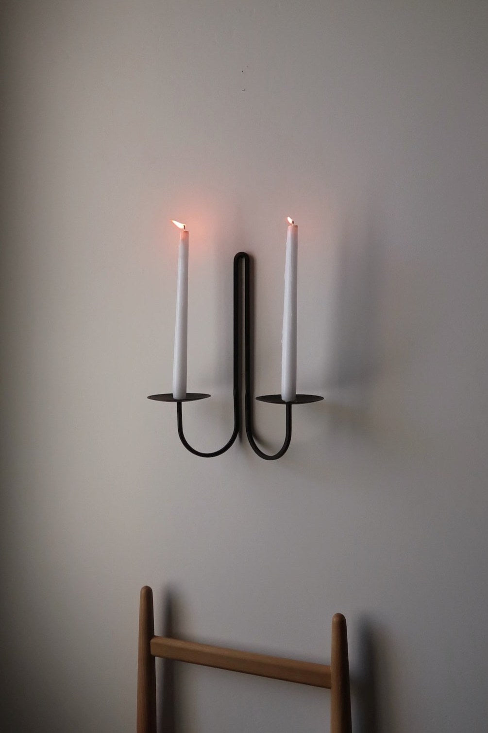 Elm double scnce with two lit candles on a plain wall.