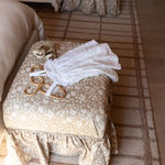 Decorative handcrafted ottoman with on a patterned rug in a bedroom and another Eloise ottoman in the background.