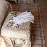 Decorative handcrafted ottoman with on a patterned rug in a bedroom and another Eloise ottoman in the background.