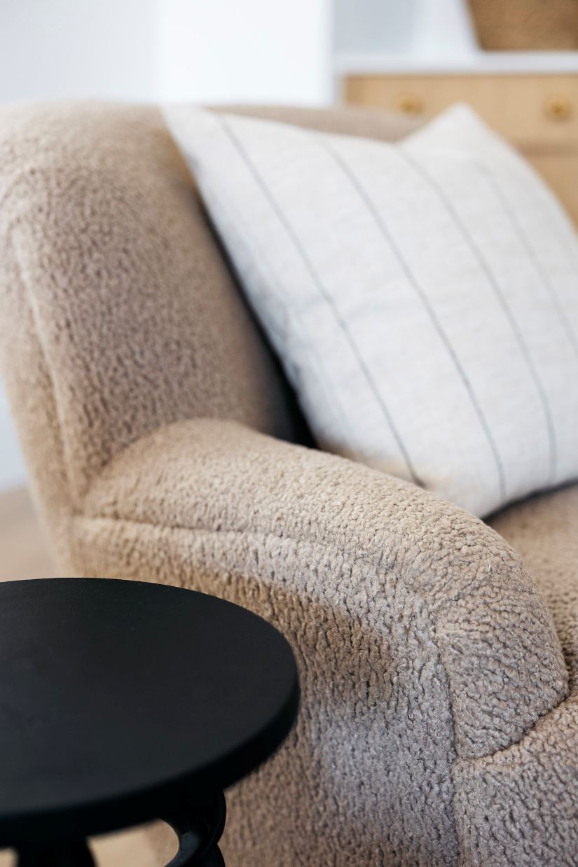 Beige textured armchair with a white cushion and a black side table.