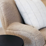 Beige textured armchair with a white cushion and a black side table.