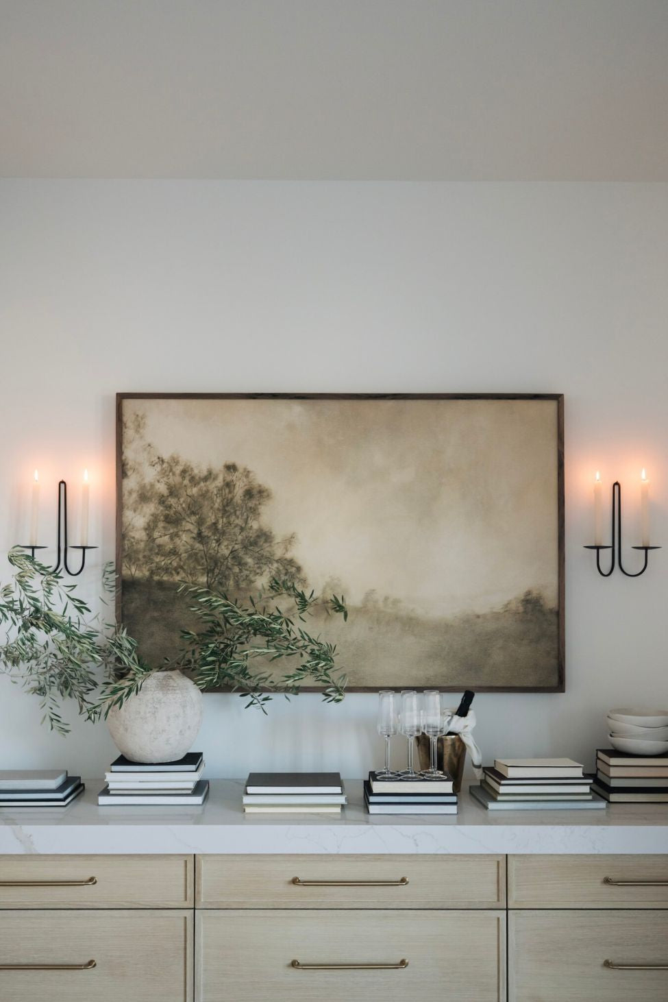 Modern interior with a large abstract landscape wall art, decorative items on a shelf, and wall sconces.