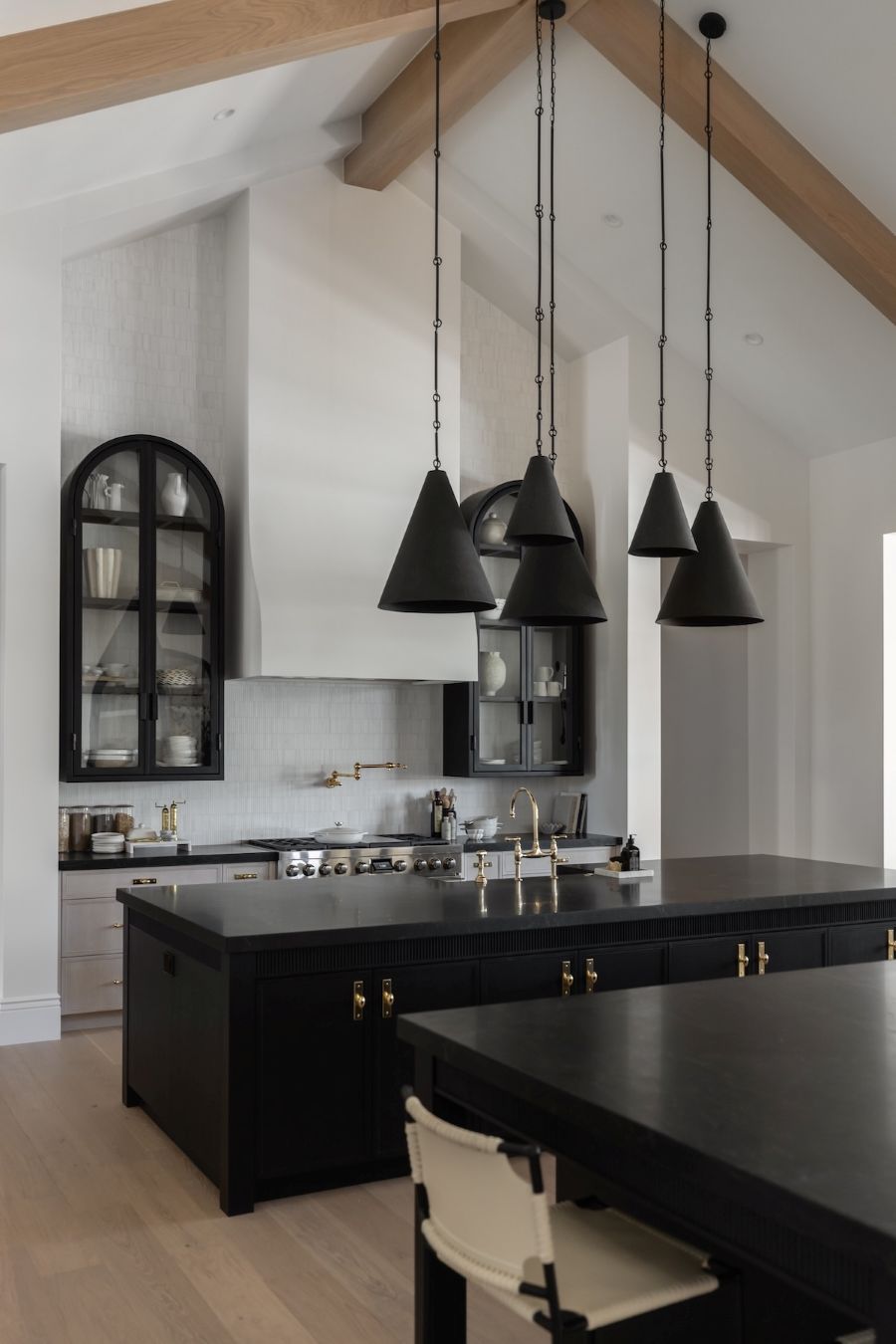 Modern kitchen with black island, black pendant lights, and white walls.