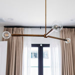 Modern chandelier with glass bulbs hanging in a room with curtains and a display cabinet.