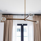Modern chandelier with glass bulbs hanging in a room with curtains and a display cabinet.