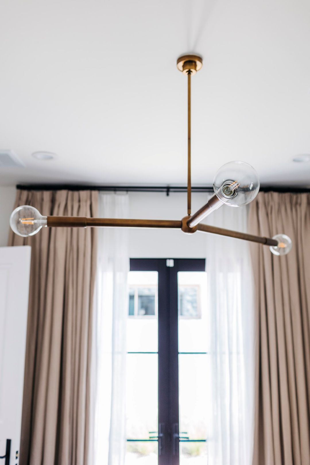 Modern chandelier with glass bulbs hanging in a room with curtains and a display cabinet.