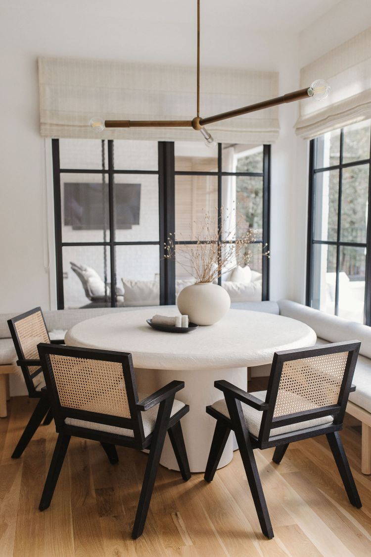 Modern dining area with a Regina Andrew Talon modern chandelier,  round white table and black chairs in a bright room.
