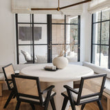 Modern dining area with a Regina Andrew Talon modern chandelier,  round white table and black chairs in a bright room.