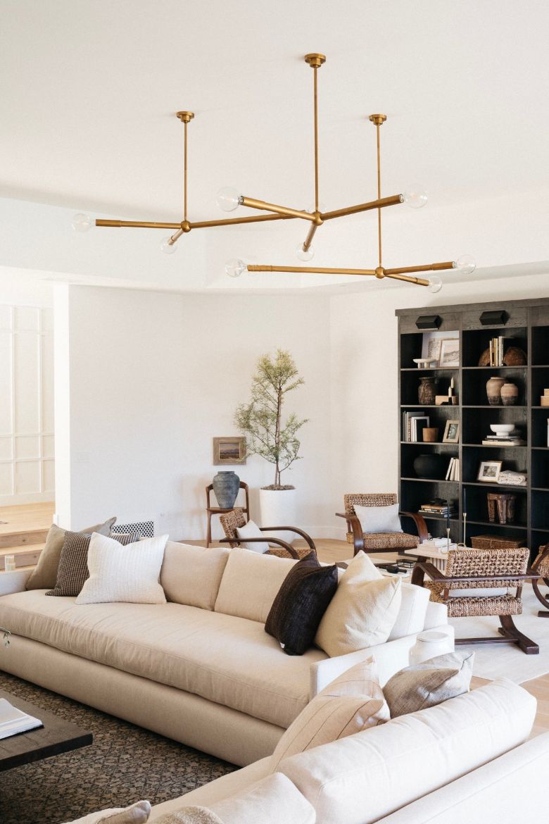 Modern living room with beige sofa, gold modern chandelier, and bookshelf.