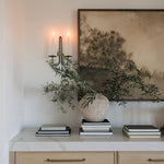 Decorative setup with a vase, books, and a framed landscape wall art on a white surface.