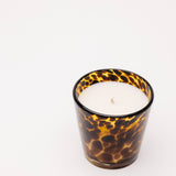 Candle in a tortoiseshell-patterned glass container on a white background