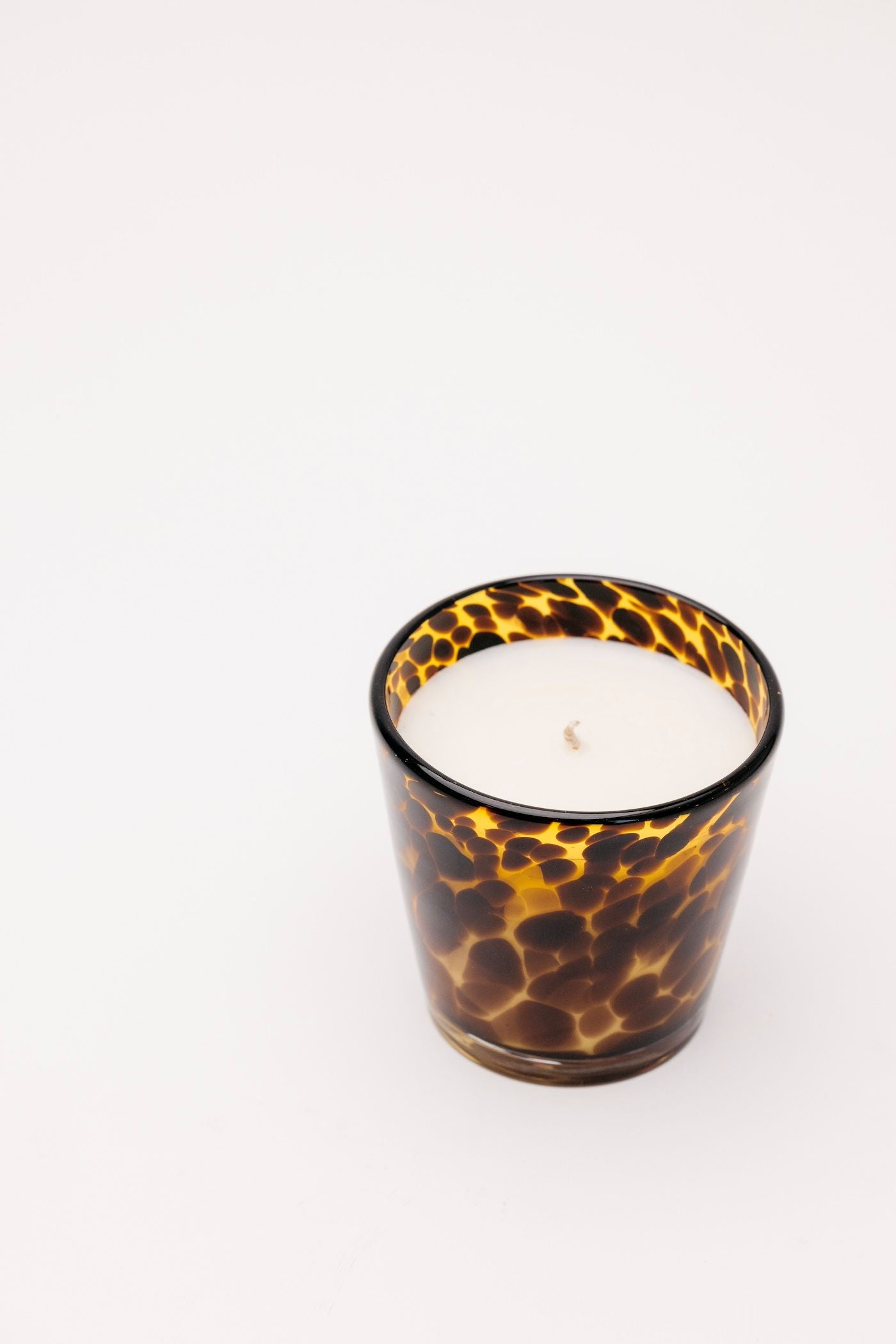 Candle in a tortoiseshell-patterned glass container on a white background