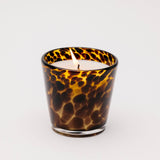 Scented candle in a tortoiseshell-patterned glass container on a white background