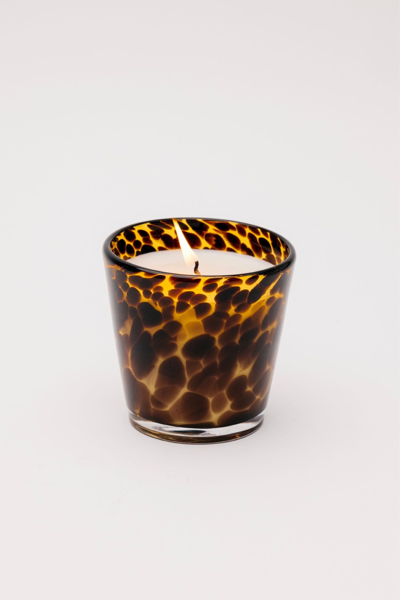 Scented candle in a tortoiseshell-patterned glass container on a white background