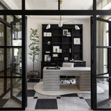 Modern office interior with a black bookshelf, unique white desk, and large glass doors.