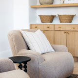 Beige armchair with a white pillow in a room with wooden shelves and cabinets.