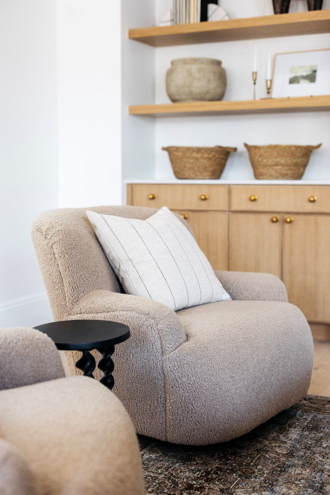 Beige armchair with a white pillow in a room with wooden shelves and cabinets.
